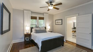 A bedroom with a bed, bedside lamps, a ceiling fan, a window with curtains, and a door leading to a closet.