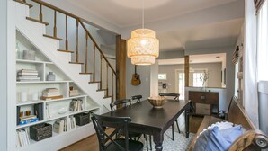 A dining area with a dark wooden table, black chairs, and a woven pendant light. A staircase with wooden railings leads to another room.