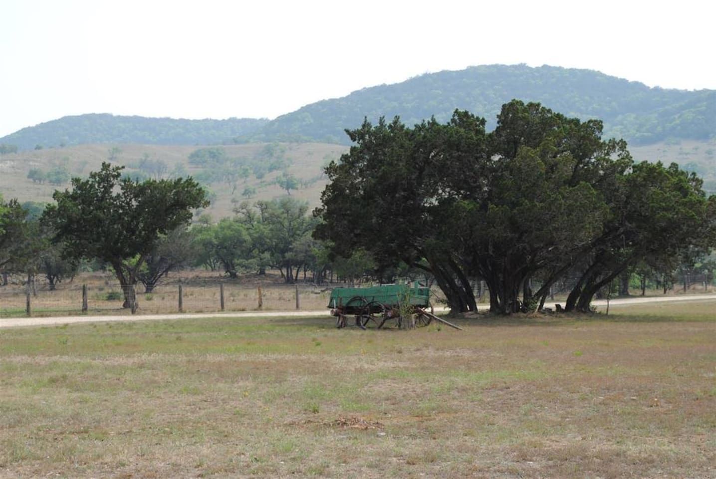 A rural landscape with a dirt road, a green cart, and a fence.