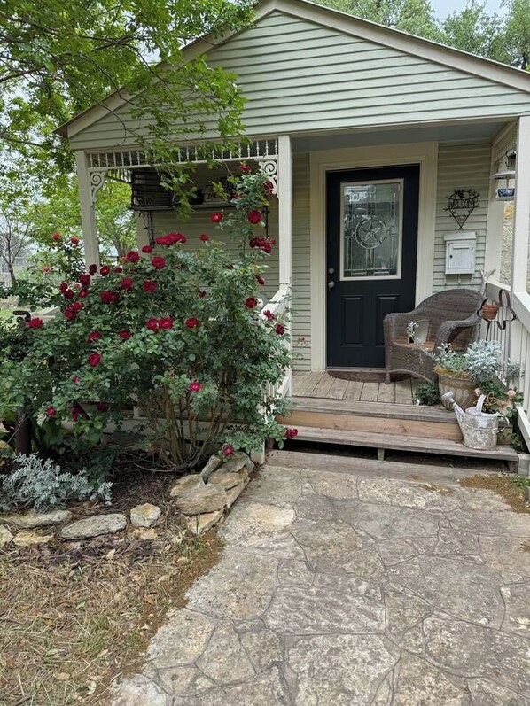 A house with a porch, a door, and a small garden area with plants and a bench.
