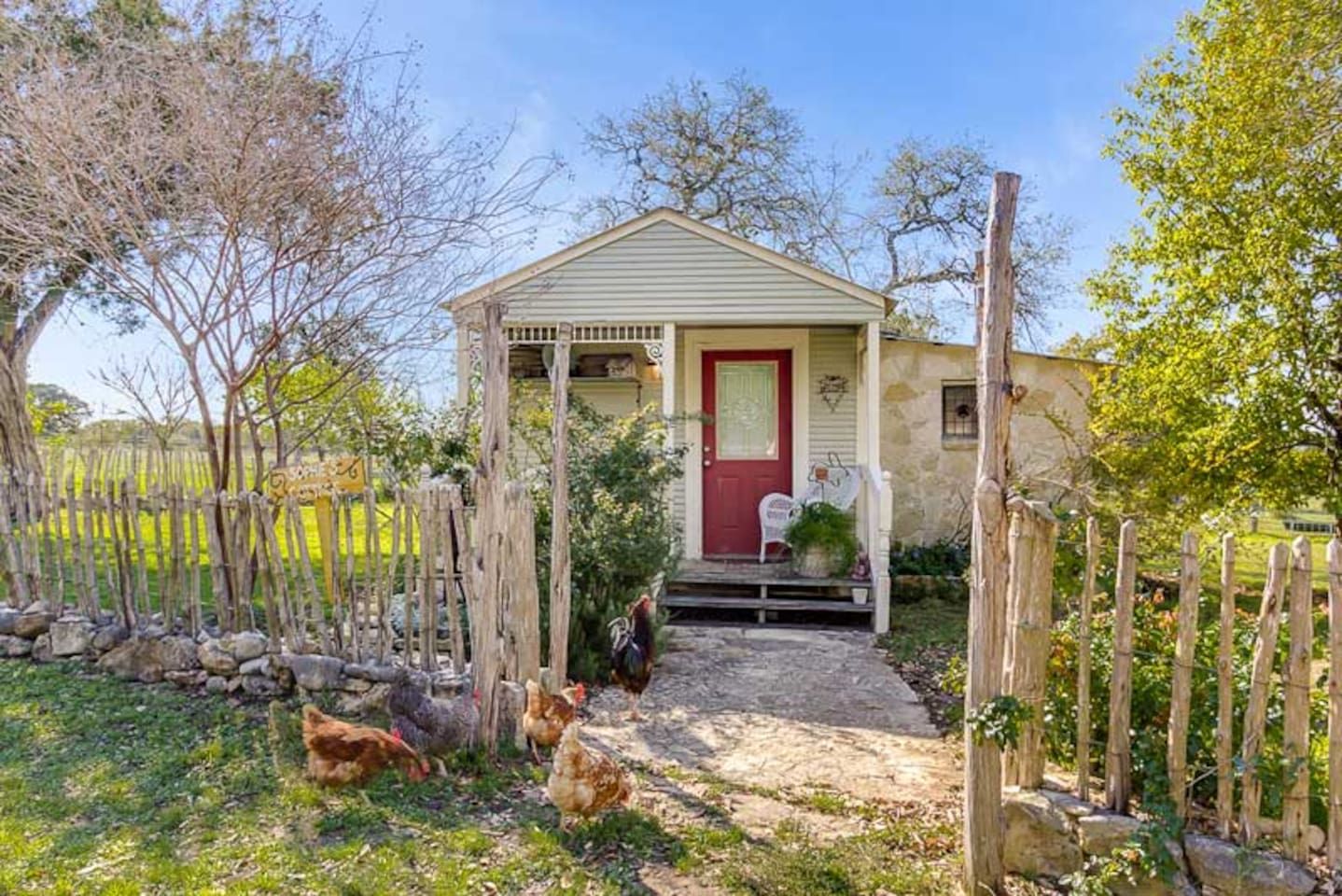 Een landelijke woning met een rode deur, een veranda en kippen in de tuin.