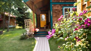 Une terrasse en bois mène à un bâtiment doté d’une porte verte et d’une chaise blanche placée à l’extérieur.