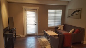A living room with a sofa, a coffee table, a TV, and a door with blinds. - Top Floor Timbers Condo in Mt. Crested Butte (Crested Butte)