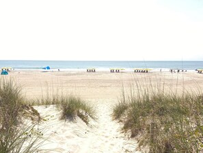 A sandy beach with tents and umbrellas, a clear sky, and a calm sea. - Oceanfront 2BR/2Bath Condo in Carolina Beach NC (Carolina Beach)