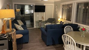 A living room with a dining area, a ceiling fan, and a kitchen visible through a glass door. - Oceanfront 2BR/2Bath Condo in Carolina Beach NC  (Carolina Beach)