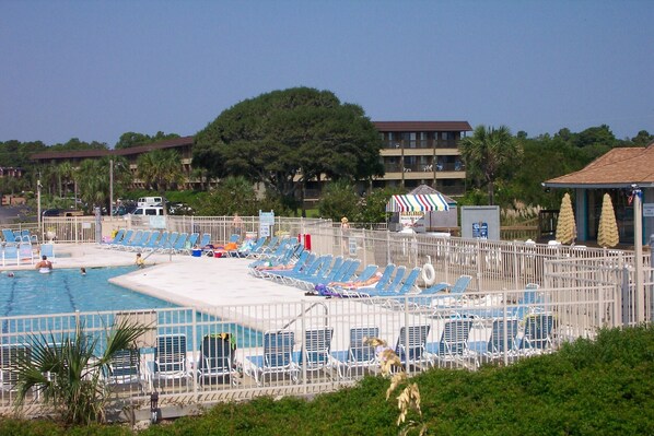 A pool area with multiple lounge chairs and a small building with a striped awning. - Ocean Front 1st Row ~ Private Corner Unit ~ Close to Pool, Beach Bar & Boardwalk (Hilton Head Island)