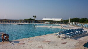 A swimming pool with blue water, a covered area with chairs, and a palm tree in the background. - Ocean Front 1st Row ~ Private Corner Unit ~ Close to Pool, Beach Bar & Boardwalk (Hilton Head Island)