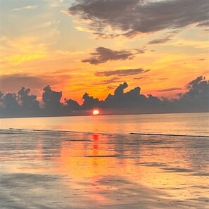 A sunset over a calm sea with a clear sky and distant land silhouettes. - Ocean Front 1st Row ~ Private Corner Unit ~ Close to Pool, Beach Bar & Boardwalk (Hilton Head Island)