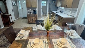 A dining area with a wooden table set for four, surrounded by chairs. A vase with greenery is placed in the center. - Top-Floor Branson Condo w/ Stunning Views & 2 King Beds (Branson)