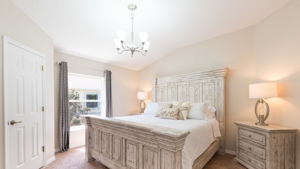 Ein Schlafzimmer mit einem großen Bett, zwei Nachttischen, einer Kristallleuchter und Blick ins Freie.