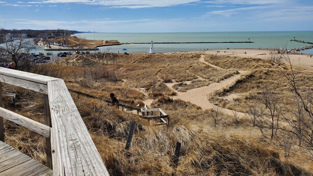 Une vue sur la côte, avec une plage de sable, un phare et une promenade en bois qui mène à l’eau.