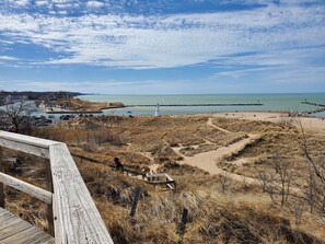 A coastal view with a sandy beach, a lighthouse, and a wooden boardwalk leading to the water. - Gorgeous Harbor Country Cottage; PRIVATE HOT TUB; close to downtown/beach (New Buffalo)