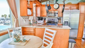 A kitchen with wooden cabinets, a stainless steel refrigerator, a microwave, and a dining area with a table and chairs. - WELCOME TO  A PARADISE GETAWAY IN WEEKI WACHEE FLORIDA (Spring Hill)