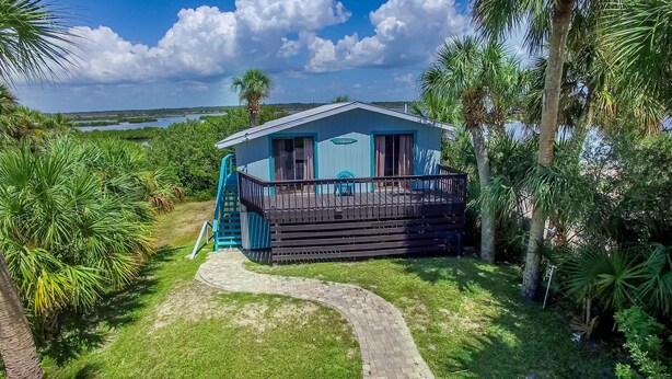 A small, single-story building with a blue exterior and a wooden deck, surrounded by lush greenery and a clear sky. - WELCOME TO  A PARADISE GETAWAY IN WEEKI WACHEE FLORIDA (Spring Hill)