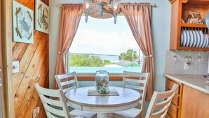 A dining area with a round table, white chairs, a view of the sea, and a wooden wall with framed pictures. - WELCOME TO  A PARADISE GETAWAY IN WEEKI WACHEE FLORIDA (Spring Hill)