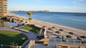 Un resort sulla spiaggia con piscina, lettini, ombrelloni e vista sul mare.