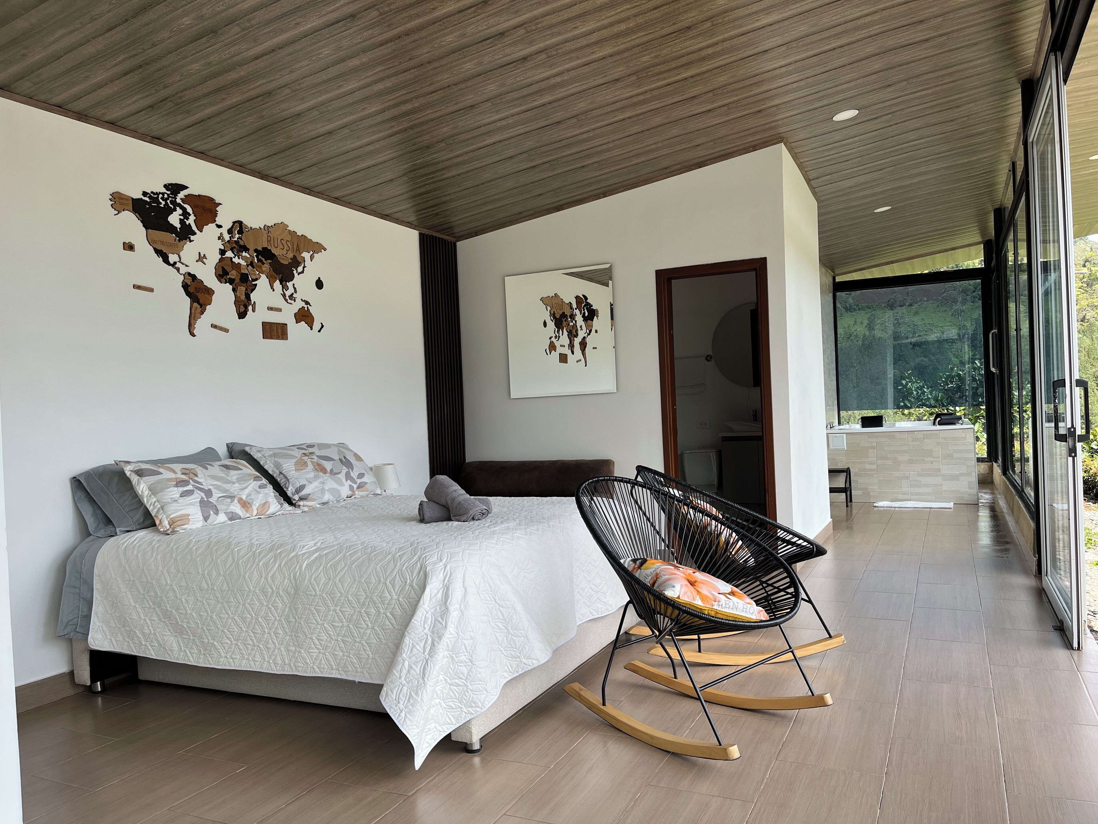 Ein modernes Schlafzimmer mit einem großen Bett, einem Schaukelstuhl und einer Weltkarte an der Wand.