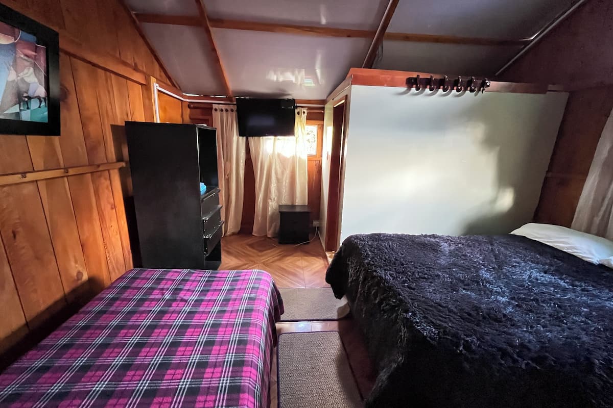 A room with two beds, wooden walls, a television, and a door leading to another room.
