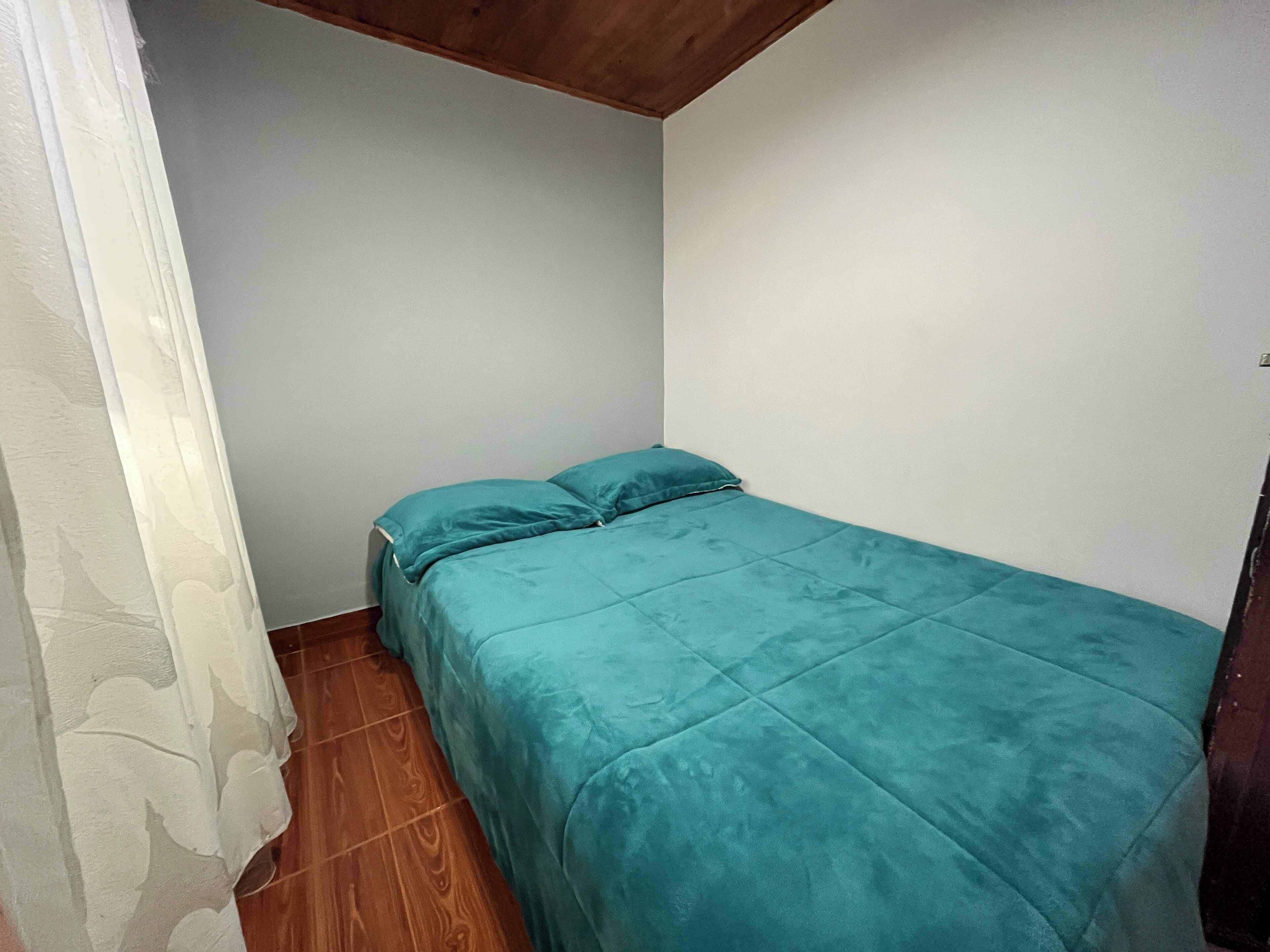 A small, single-bed room with a teal bedspread and white walls.