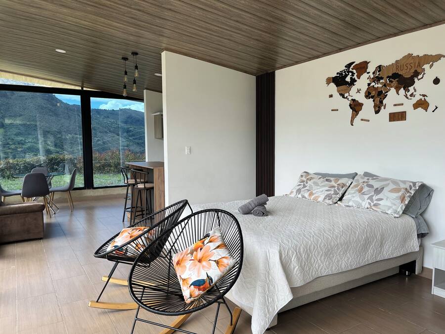 Un dormitorio moderno con una cama grande, un mural de un mapa mundial, una zona de comedor con sillas y vistas al exterior.