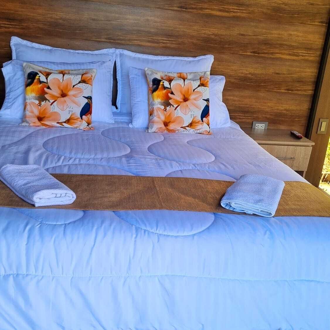 A neatly made bed with floral pillows, a wooden headboard, and a wooden nightstand with a remote control.