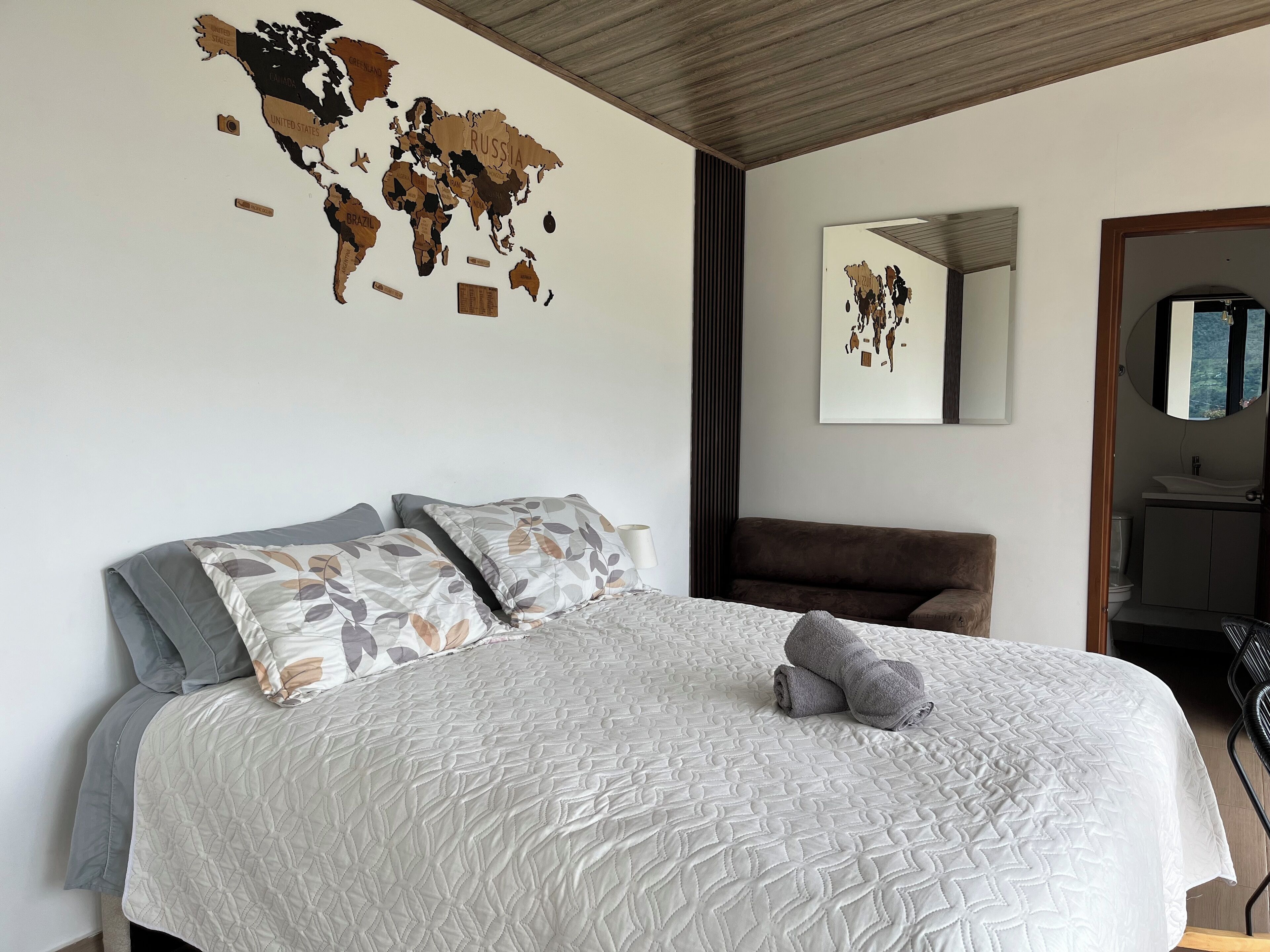 Cama bem arrumada com cobertura branca acolchoada, um quadro de parede com um mapa-múndi e teto de madeira.