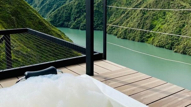 A bathtub with a view of a river and mountains.