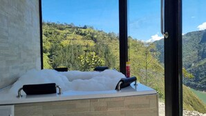 A bathroom with a large bathtub filled with bubbles, a black towel, and a bottle of shampoo. The bathroom has a view of a mountainous landscape.