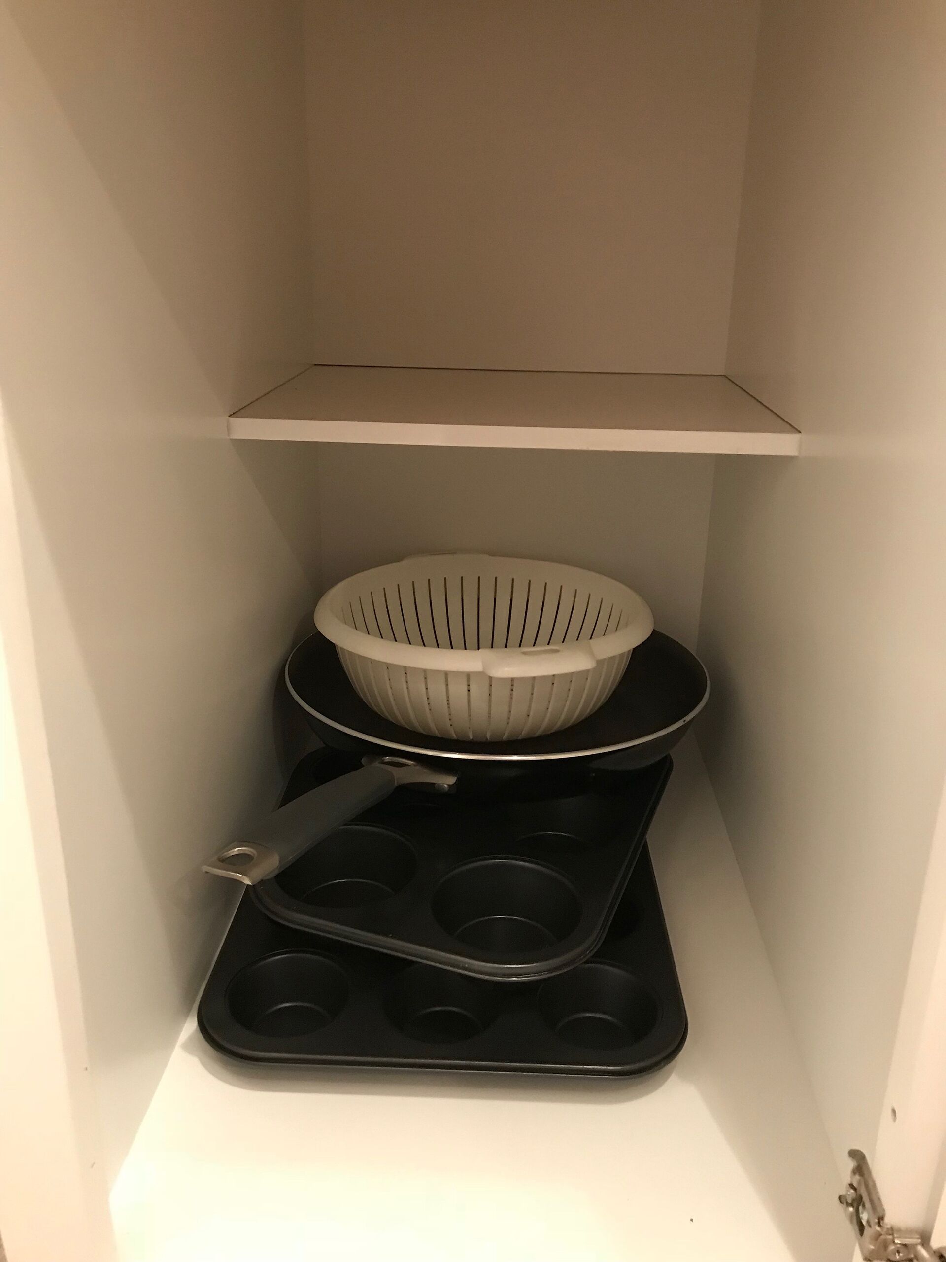 Una cocina con un estante blanco, un colador blanco y una bandeja negra para muffins.