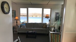 Un salon avec un canapé, une table basse et une vue sur un lac. Il y a une lampe et une horloge au mur.
