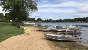 Une plage de sable fin, avec une chaise jaune et un canot à rames baptisé « Sea Nymph », amarré au bord de l’eau.