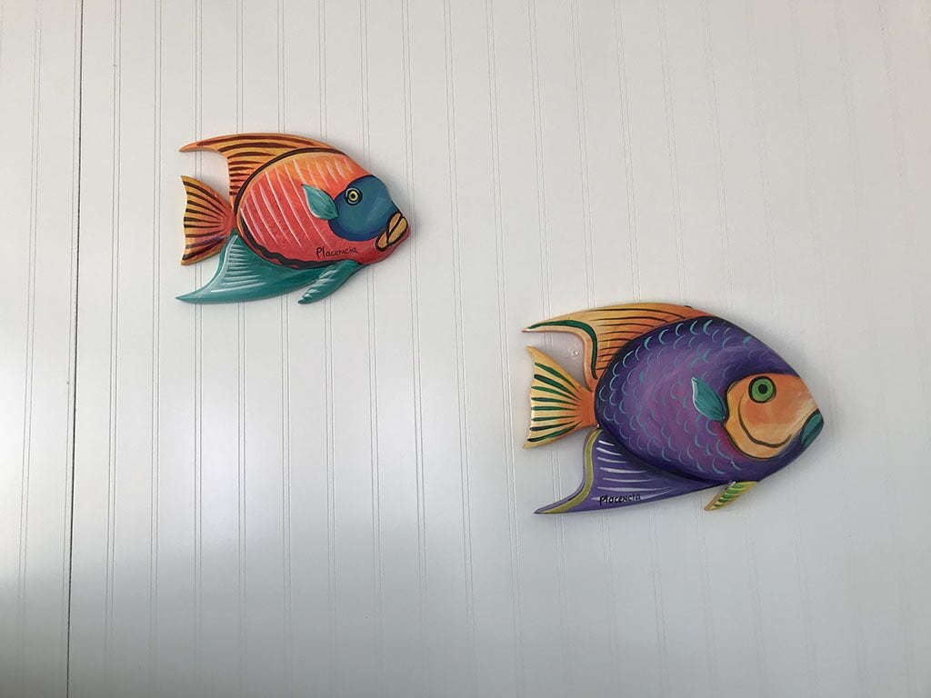 Two colorful fish wall art pieces on a white wall.