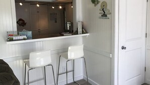 Une cuisine avec des tabourets de bar blancs, une porte blanche et des œuvres d’art décoratives au mur.
