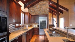 A modern kitchen with wooden cabinets, a stone backsplash, and a built-in oven. - Elk Run-Hot Tub, Pet Friendly, and Close to Slopes (Mt Crested Butte)