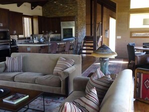 Ein geräumiger Wohnbereich mit Sofa, Sesseln und Couchtisch, im Hintergrund eine Küche und ein Essbereich mit Stühlen.