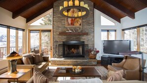 A living room with a stone fireplace, a television, and large windows. - Elk Run-Hot Tub, Pet Friendly, and Close to Slopes (Mt Crested Butte)