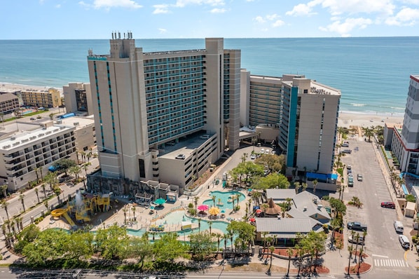 A hotel with multiple floors, a swimming pool area, and a view of the beach.