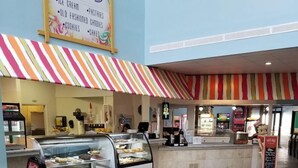 Una panadería con un toldo a rayas de colores y una vitrina llena de diversos productos horneados.