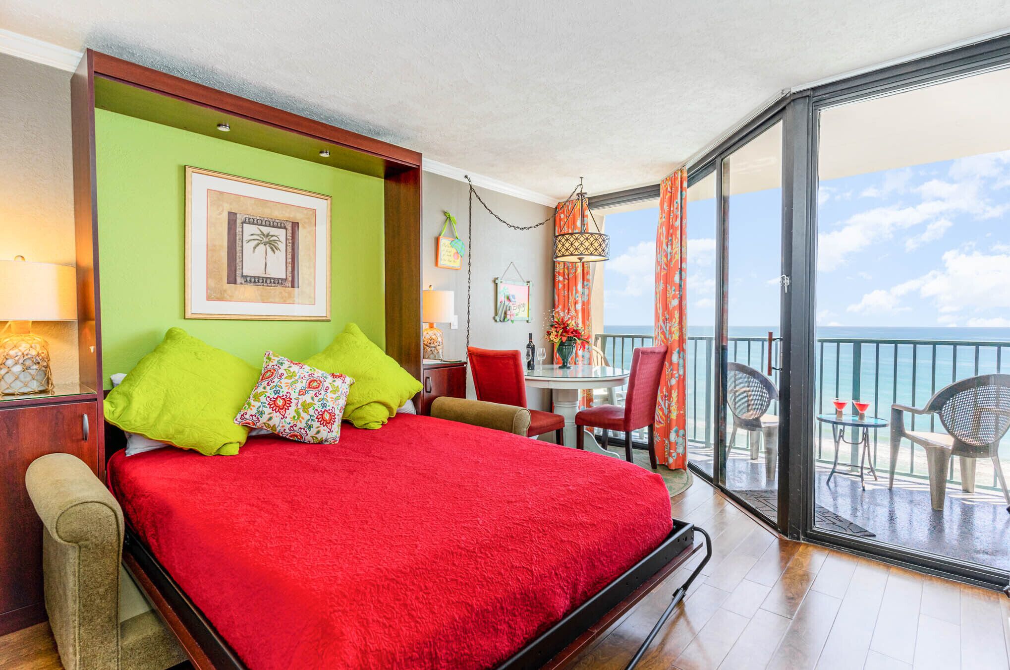 A room with a large bed, a balcony with a view of the sea, and a table with chairs.