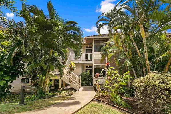 A two-story building with a balcony, surrounded by lush greenery and palm trees.