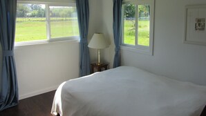 A bedroom with two windows, a bed, a nightstand, and a lamp.