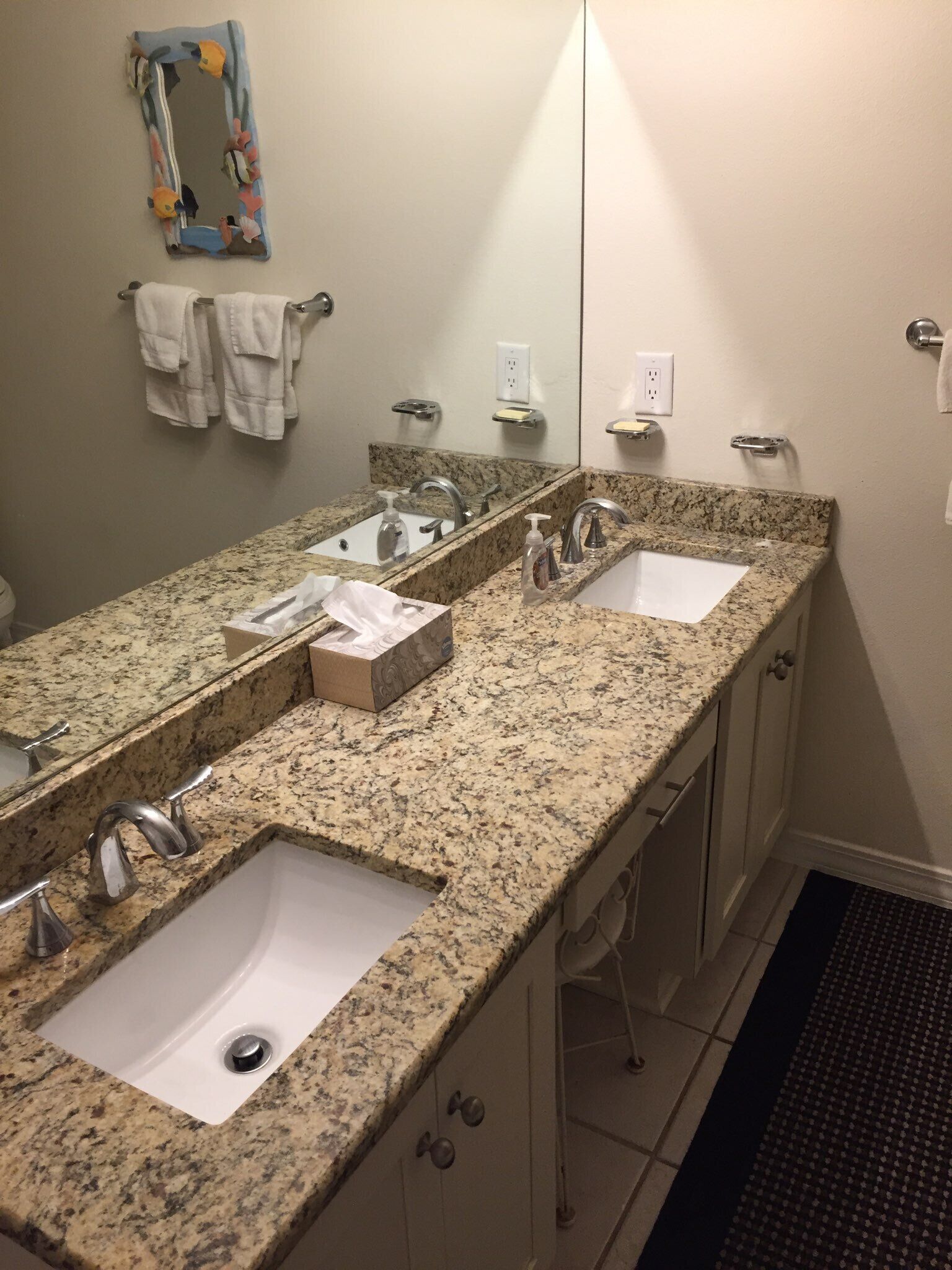 A bathroom with a granite countertop, two sinks, a large mirror, and a towel rack.