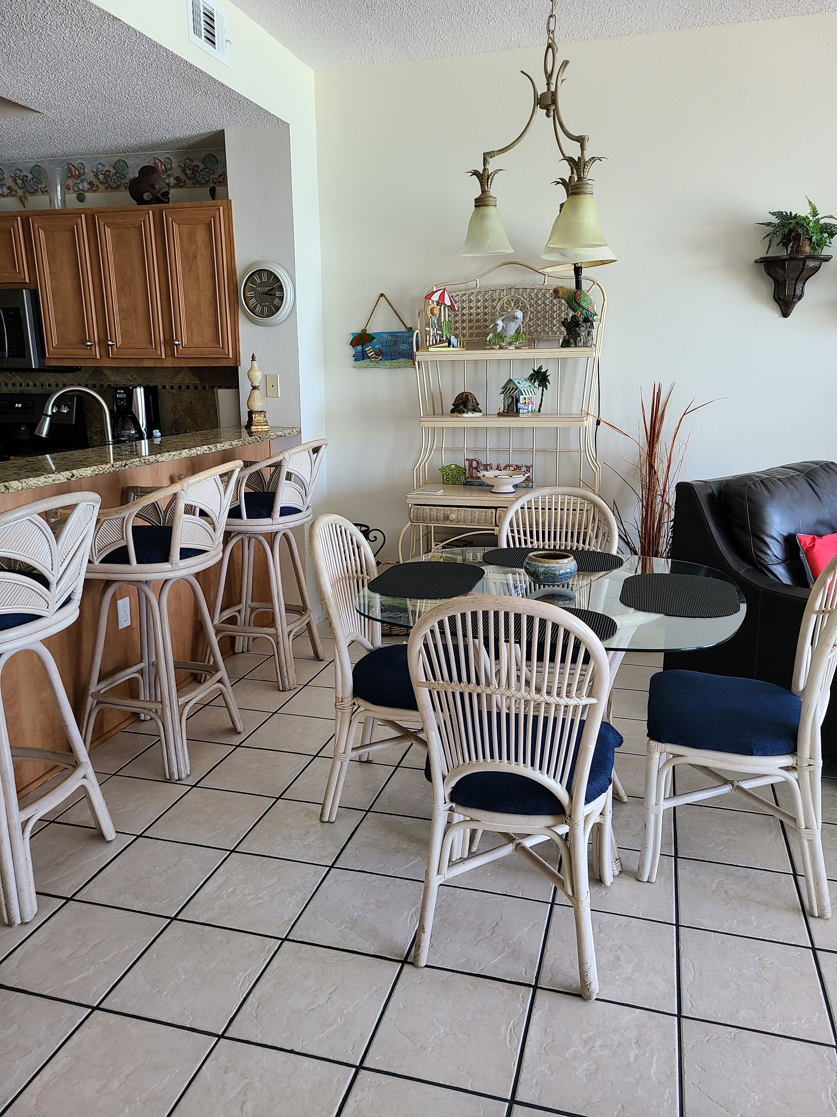 Un comedor con sillas de mimbre y una mesa de vidrio, una cocina con armarios de madera y un estante decorativo con plantas.