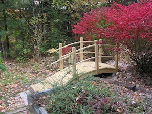 Cross a serene wooden bridge over a tranquil stream surrounded by lush greenery.