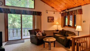 A cozy living room with a fireplace, large windows, and a wooden ceiling.