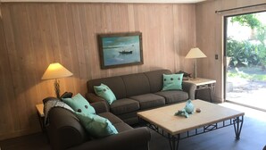 Un salon avec un canapé marron, des coussins turquoise, une table basse et un tableau représentant un bateau accroché au mur.