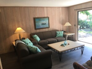 Een woonkamer met een bruine bank, kussens in blauwgroen, een salontafel en een schilderij van een boot aan de muur.