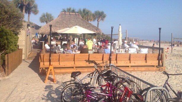 Un restaurant situé en bord de mer, doté d’une terrasse, d’un toit de chaume et de vélos garés devant.