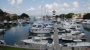 Un port de plaisance où sont amarrés de nombreux bateaux, un phare en arrière-plan et des bâtiments le long de la promenade.