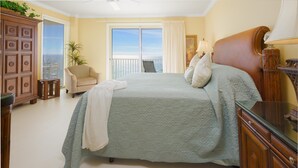 Ein Schlafzimmer mit einem großen Bett, Meerblick, einem Sessel und einer Holzkommode.